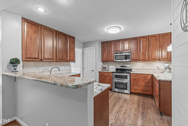 208 Silk Hope Dr, Cary, NC 27519 - kitchen with appliances with stainless steel finishes, a peninsula, light wood-style floors, brown cabinetry, and decorative backsplash