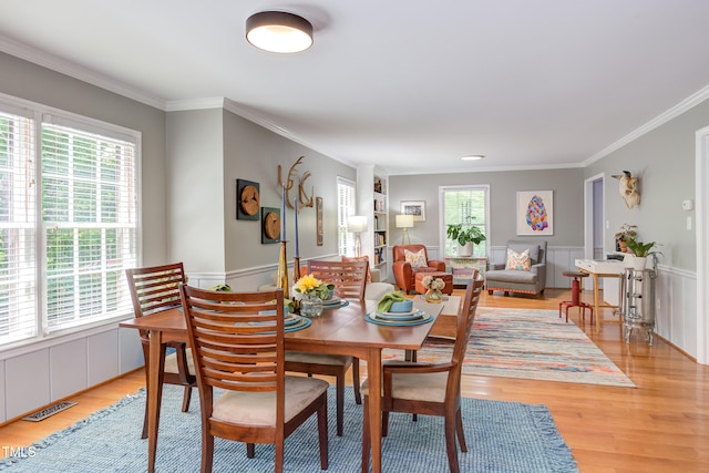 dining space featuring light wood finished floors, ornamental molding, and a wainscoted wall