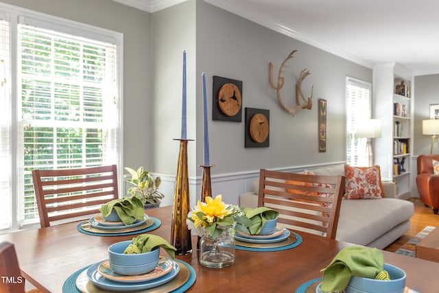 dining space featuring crown molding, built in shelves, wood finished floors, and a wainscoted wall