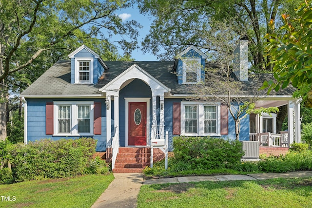 new england style home featuring a chimney, a front lawn, and covered porch