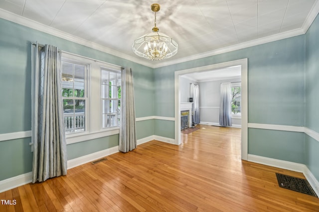 empty room with a chandelier, light wood finished floors, plenty of natural light, a fireplace with flush hearth, and ornamental molding