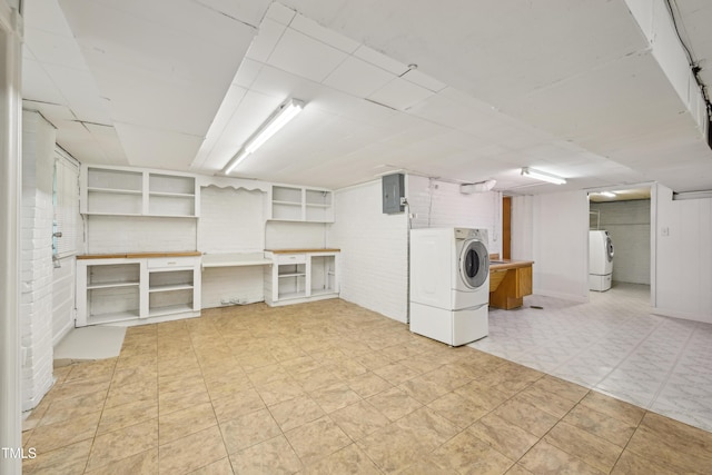 finished below grade area with washer / dryer, light floors, brick wall, and electric panel
