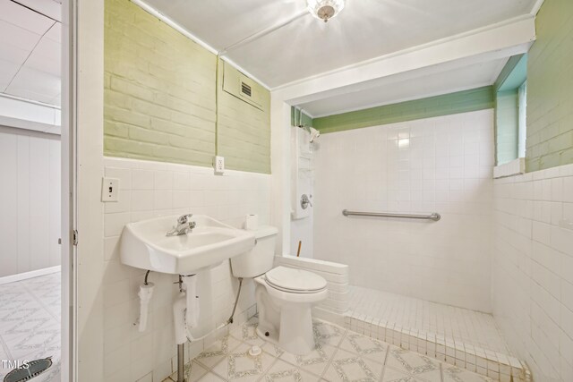 bathroom featuring tiled shower, toilet, tile walls, and wainscoting