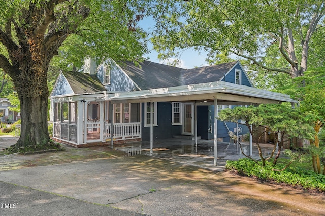 view of front of property with an attached carport, a sunroom, driveway, and a shingled roof