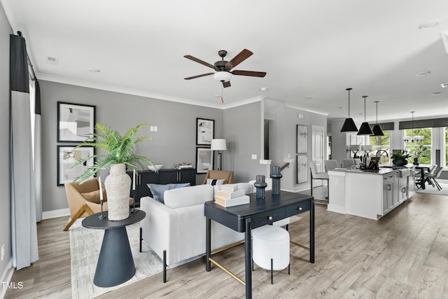living room featuring light wood-style floors, a ceiling fan, baseboards, and crown molding