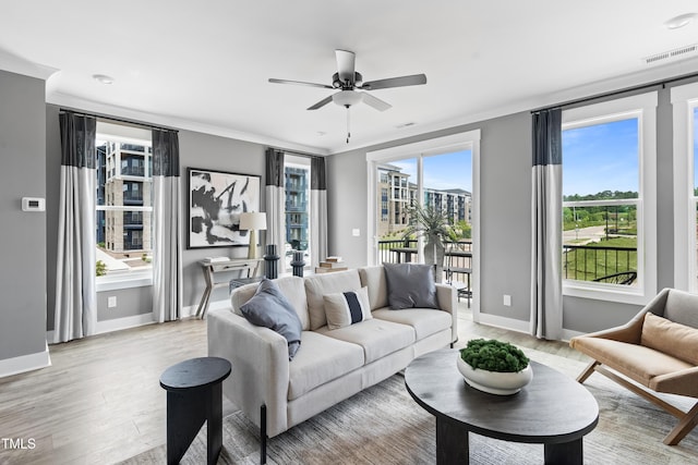 living area featuring light wood finished floors, a ceiling fan, baseboards, and crown molding