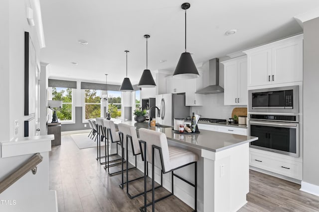 kitchen with appliances with stainless steel finishes, wall chimney exhaust hood, a spacious island, backsplash, and white cabinetry