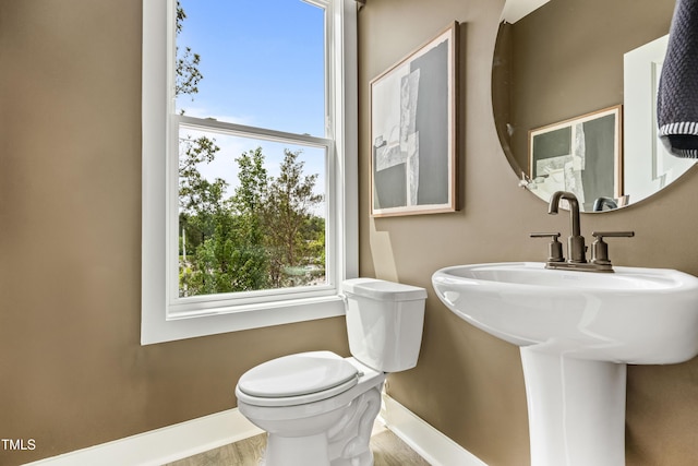 half bathroom with baseboards, toilet, and wood finished floors