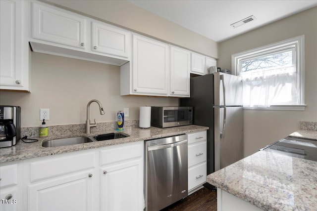 kitchen with stainless steel appliances, a sink, white cabinets, and light stone countertops