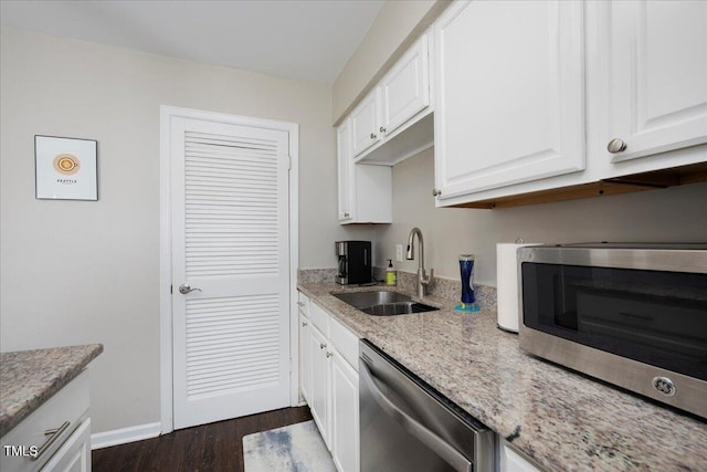 kitchen featuring stainless steel appliances, a sink, white cabinets, dark wood-style flooring, and light stone counters