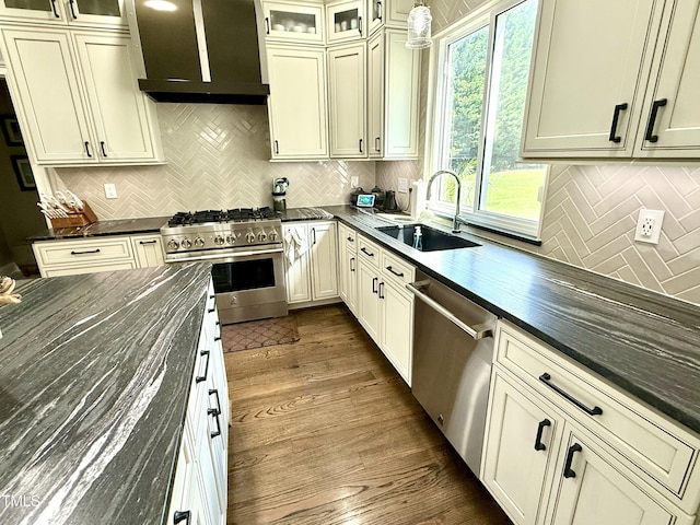 kitchen with stainless steel appliances, a sink, wall chimney exhaust hood, and decorative backsplash