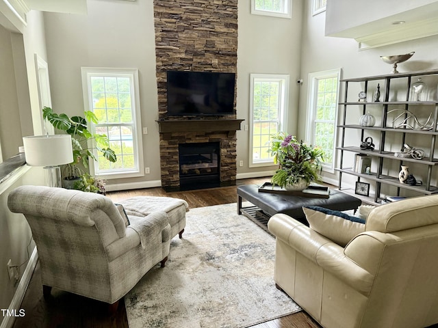 living area with wood finished floors, a stone fireplace, baseboards, and a high ceiling