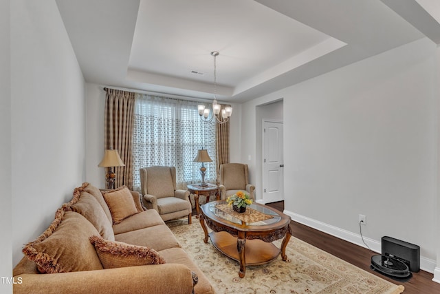 living area featuring a chandelier, a tray ceiling, baseboards, and dark wood-style floors