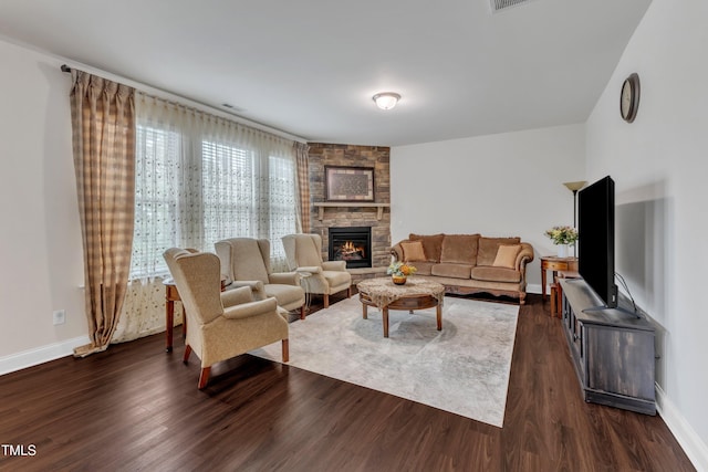 living room featuring a stone fireplace, dark wood-type flooring, and baseboards