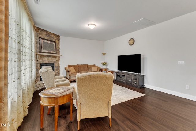 living room featuring a stone fireplace, baseboards, and dark wood-style floors