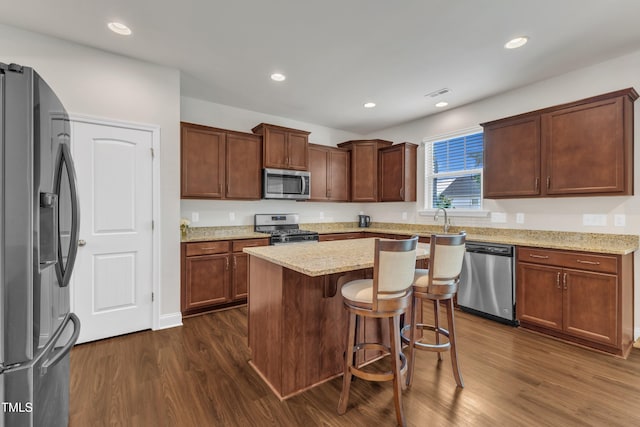 kitchen with appliances with stainless steel finishes, dark wood-style floors, light stone countertops, a center island, and recessed lighting