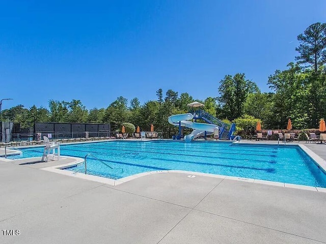 community pool with a water slide, a patio, and fence