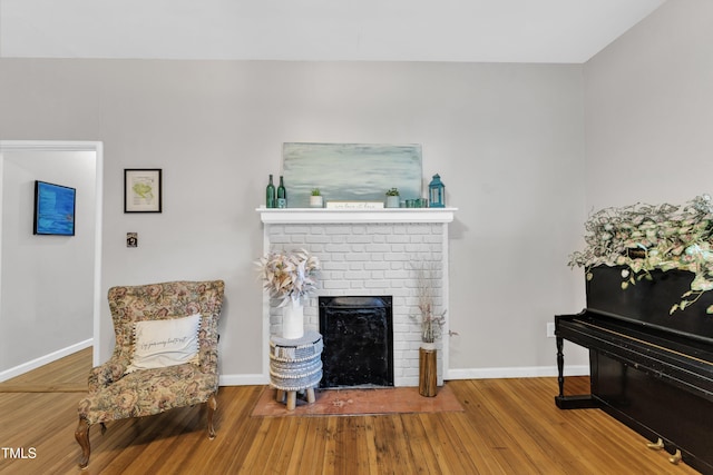 living room with wood finished floors, baseboards, and a brick fireplace