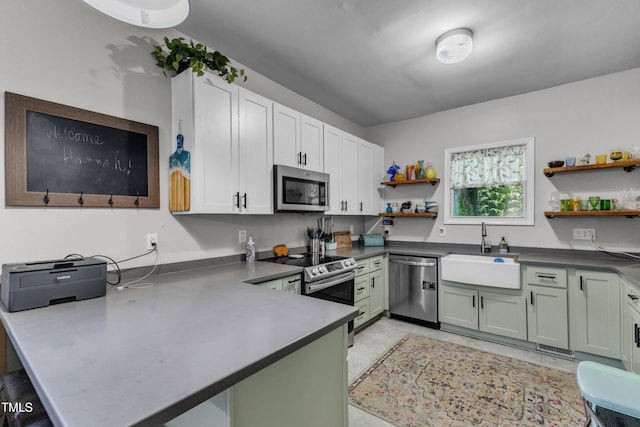 kitchen with appliances with stainless steel finishes, open shelves, a sink, a peninsula, and dark countertops