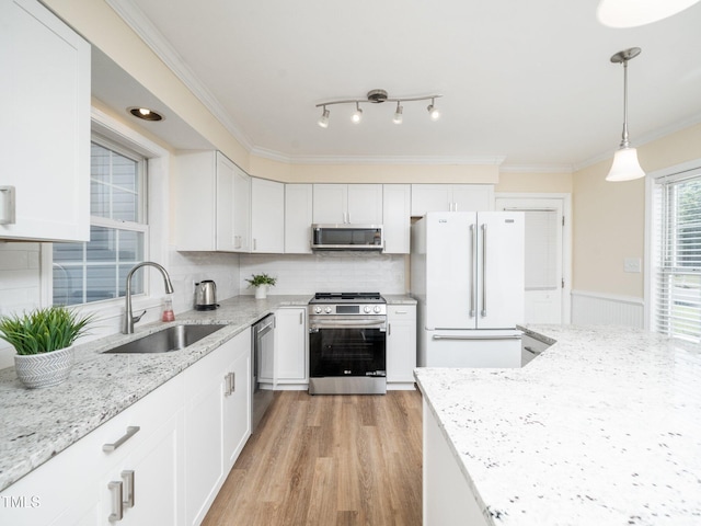 kitchen featuring appliances with stainless steel finishes, a sink, ornamental molding, light wood finished floors, and white cabinetry