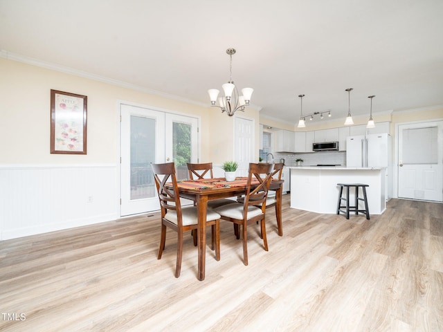 dining space with light wood finished floors, a chandelier, rail lighting, crown molding, and wainscoting