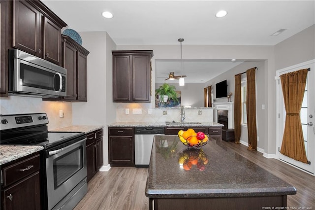 kitchen with stainless steel appliances, a sink, light wood-style floors, dark brown cabinetry, and tasteful backsplash