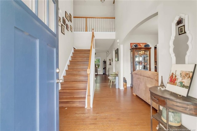 entryway featuring a high ceiling, arched walkways, stairs, and wood finished floors