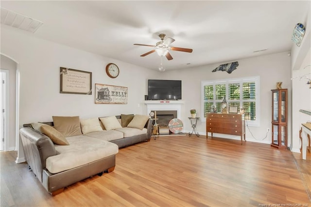 living area featuring a ceiling fan, light wood finished floors, arched walkways, a fireplace, and baseboards