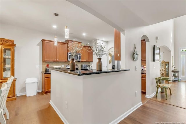 kitchen with stainless steel microwave, arched walkways, light wood-style floors, decorative backsplash, and recessed lighting
