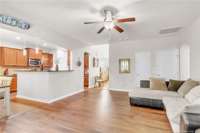 living area with arched walkways, a ceiling fan, light wood-style floors, baseboards, and recessed lighting