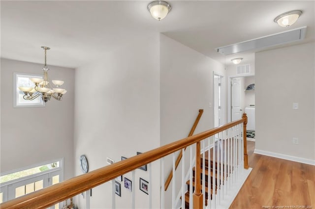 hall with attic access, an upstairs landing, light wood-style floors, a chandelier, and baseboards