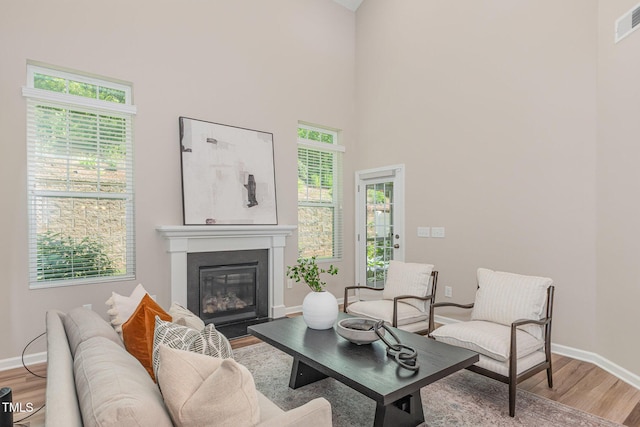 living area with light wood-type flooring, baseboards, a high ceiling, and a glass covered fireplace
