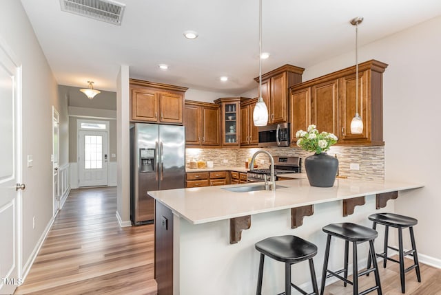 kitchen with stainless steel appliances, brown cabinets, a peninsula, light wood-style flooring, and glass insert cabinets
