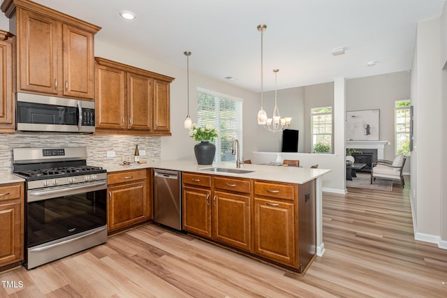 kitchen featuring appliances with stainless steel finishes, a sink, a peninsula, brown cabinets, and recessed lighting