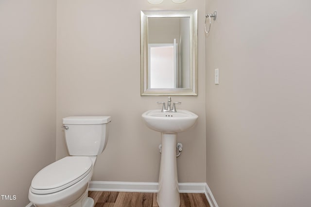 half bath featuring wood finished floors, toilet, and baseboards
