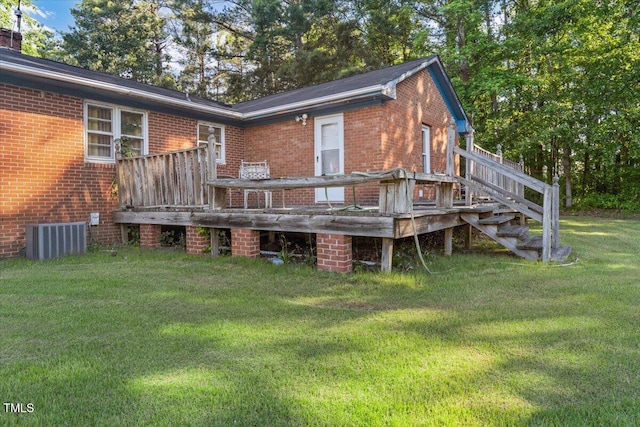 back of property with brick siding, a lawn, a wooden deck, and central AC