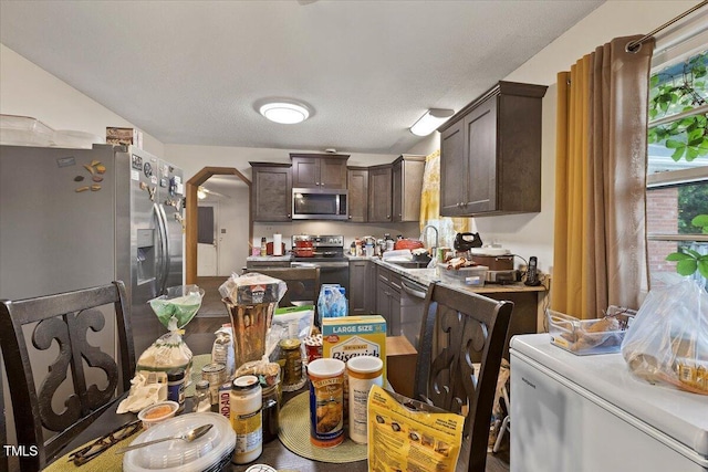 kitchen featuring appliances with stainless steel finishes, dark brown cabinets, a sink, light countertops, and arched walkways