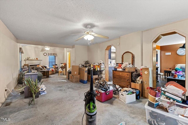living room with arched walkways, ceiling fan, carpet floors, a textured ceiling, and a fireplace