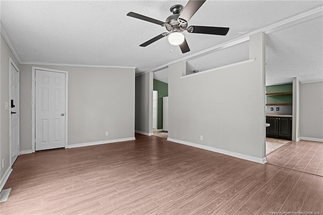 spare room with ceiling fan, crown molding, wood finished floors, a textured ceiling, and baseboards