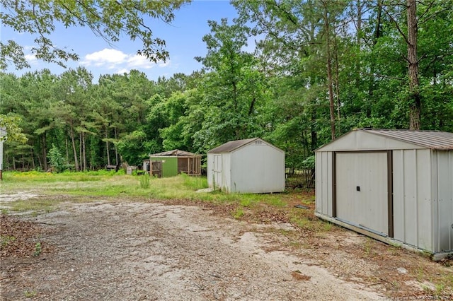 view of yard featuring a storage unit, an outdoor structure, and a wooded view