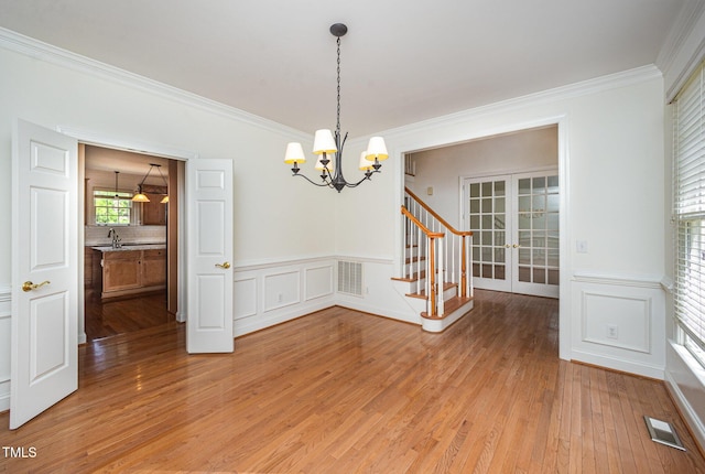 spare room featuring french doors, a chandelier, ornamental molding, light wood finished floors, and a wainscoted wall