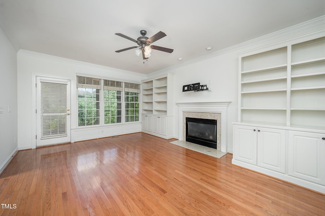 unfurnished living room featuring ornamental molding, a fireplace, a ceiling fan, light wood finished floors, and built in shelves