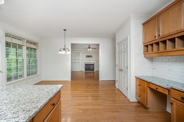 kitchen featuring crown molding, decorative backsplash, a glass covered fireplace, light wood-style floors, and a chandelier