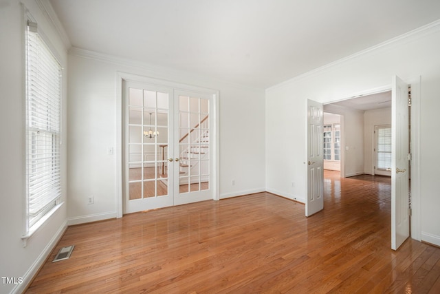 spare room with french doors, light wood finished floors, crown molding, baseboards, and a chandelier