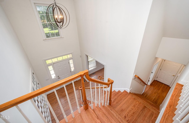 stairway with wood finished floors, a chandelier, a towering ceiling, and baseboards