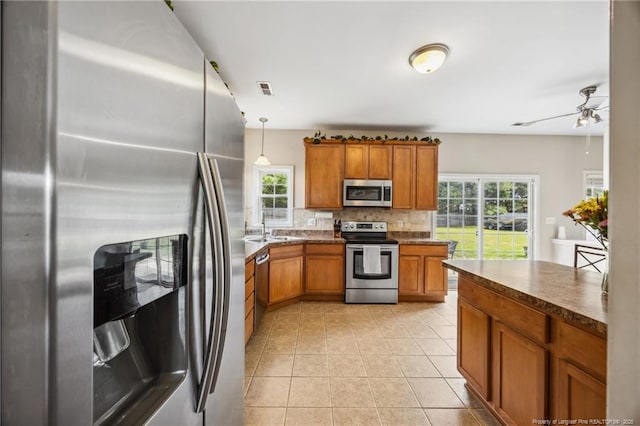 kitchen with appliances with stainless steel finishes, brown cabinetry, tasteful backsplash, and plenty of natural light