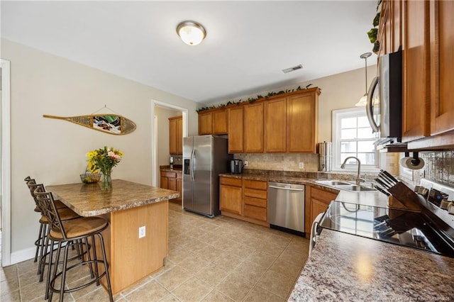 kitchen with stainless steel appliances, a sink, brown cabinets, a breakfast bar, and tasteful backsplash