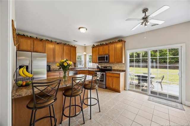 kitchen with appliances with stainless steel finishes, brown cabinetry, backsplash, and a breakfast bar area