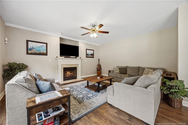 living area with a ceiling fan, wood finished floors, crown molding, a warm lit fireplace, and baseboards