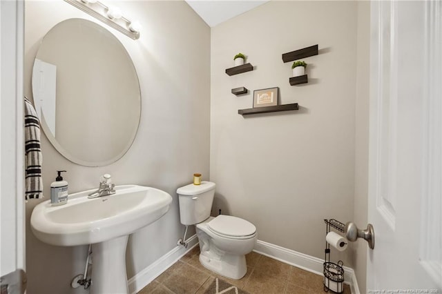 half bath with baseboards, toilet, and tile patterned floors